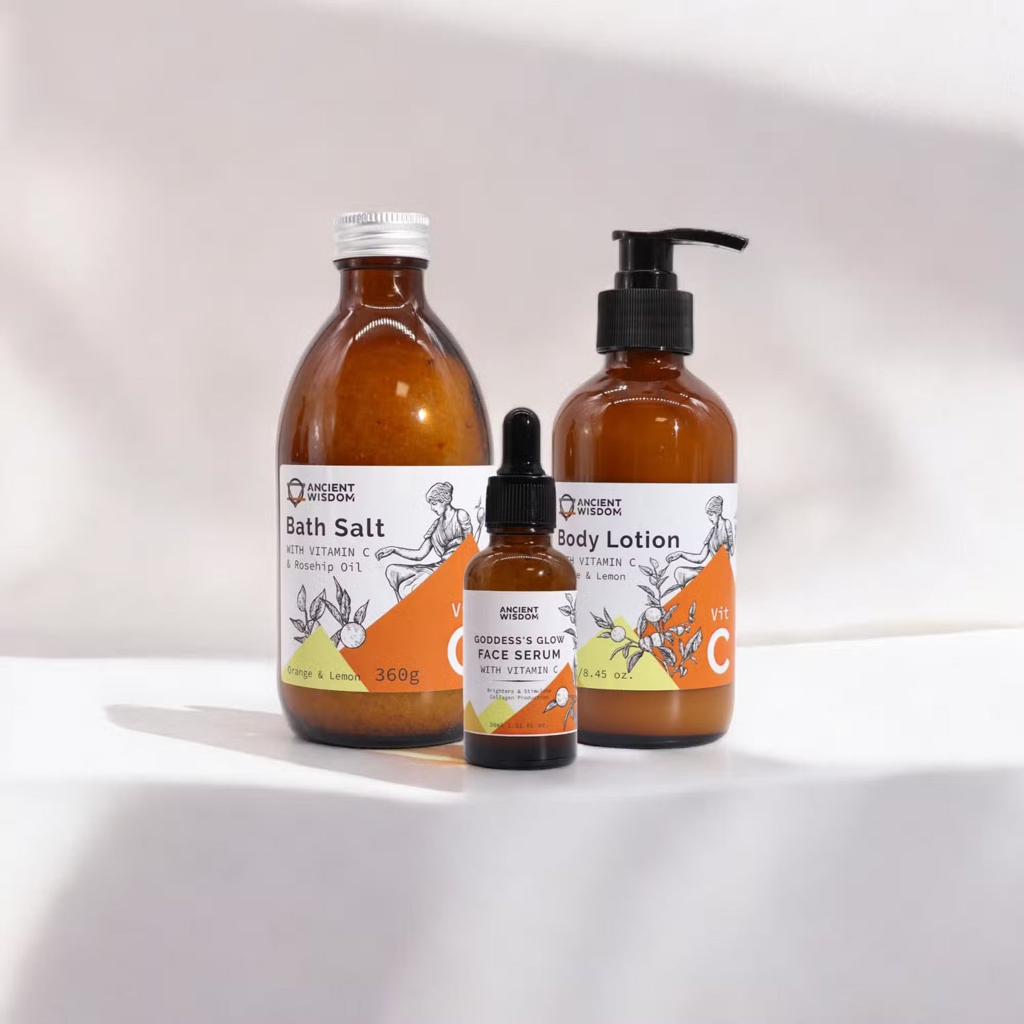 Vitamin C skincare set, Vitamin C Goddess's Glow Ritual three amber bottles in different sizes on a pale from Quintessential Holistic Health.