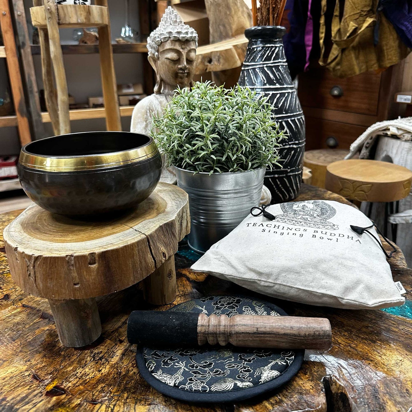 Side View of the 14 cm Hand Beaten & Engraved Singing Bowl Gift Set Sitting on a table surrounded by Buddha and decorative Spiritual Ornaments.
