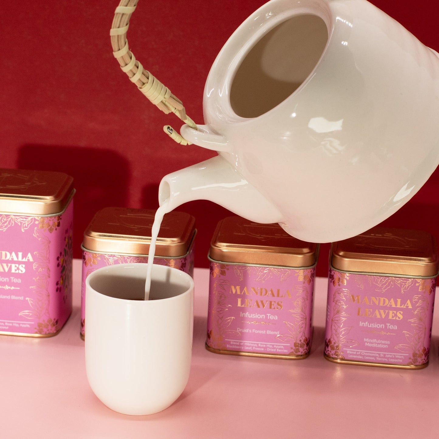 Mindfulness Meditation Blend Artisan Tea - Tinned - 50g in pink tins behind a white cup as liquid pours from a white teapot by Quintessential Holistic Health Ltd
