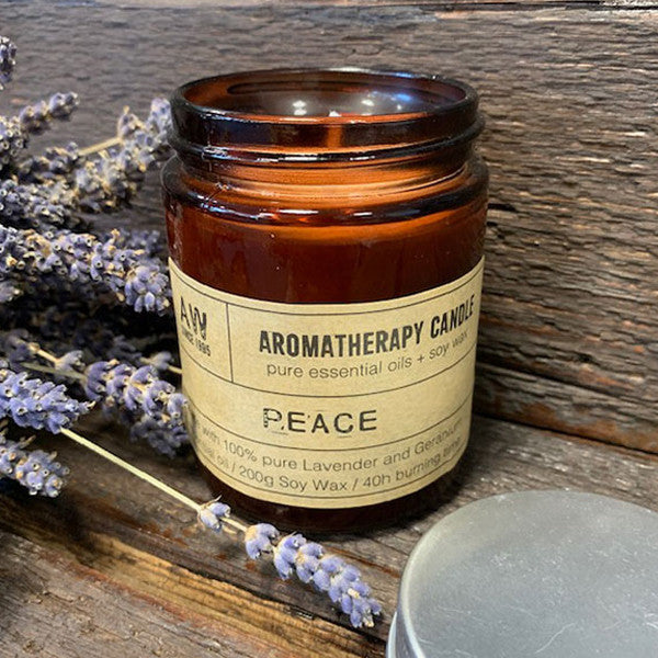 Soy Wax Candle - Peace - Lavender & Geranium, lit in an open amber jar beside lavender stems by Quintessential Holistic Health Ltd