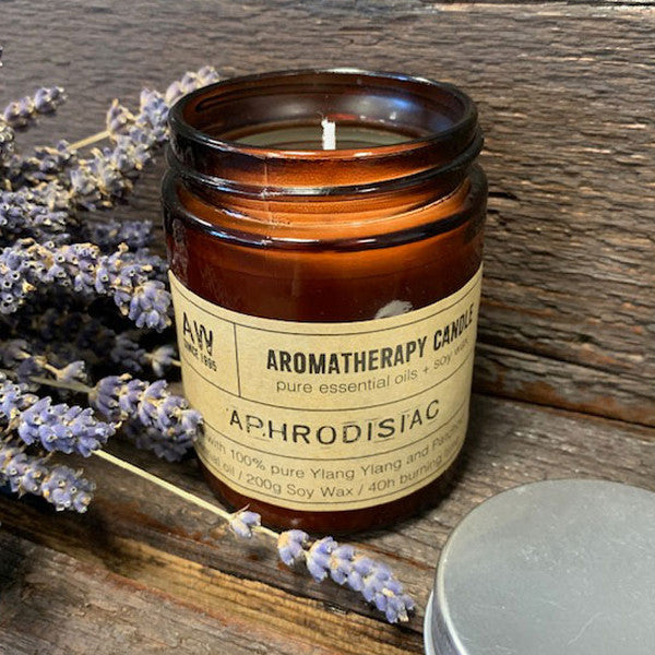Soy Wax Candle - Aphrodisiac - Ylang Ylang & Patchouli, lit in an open amber jar beside lavender stems by Quintessential Holistic Health Ltd