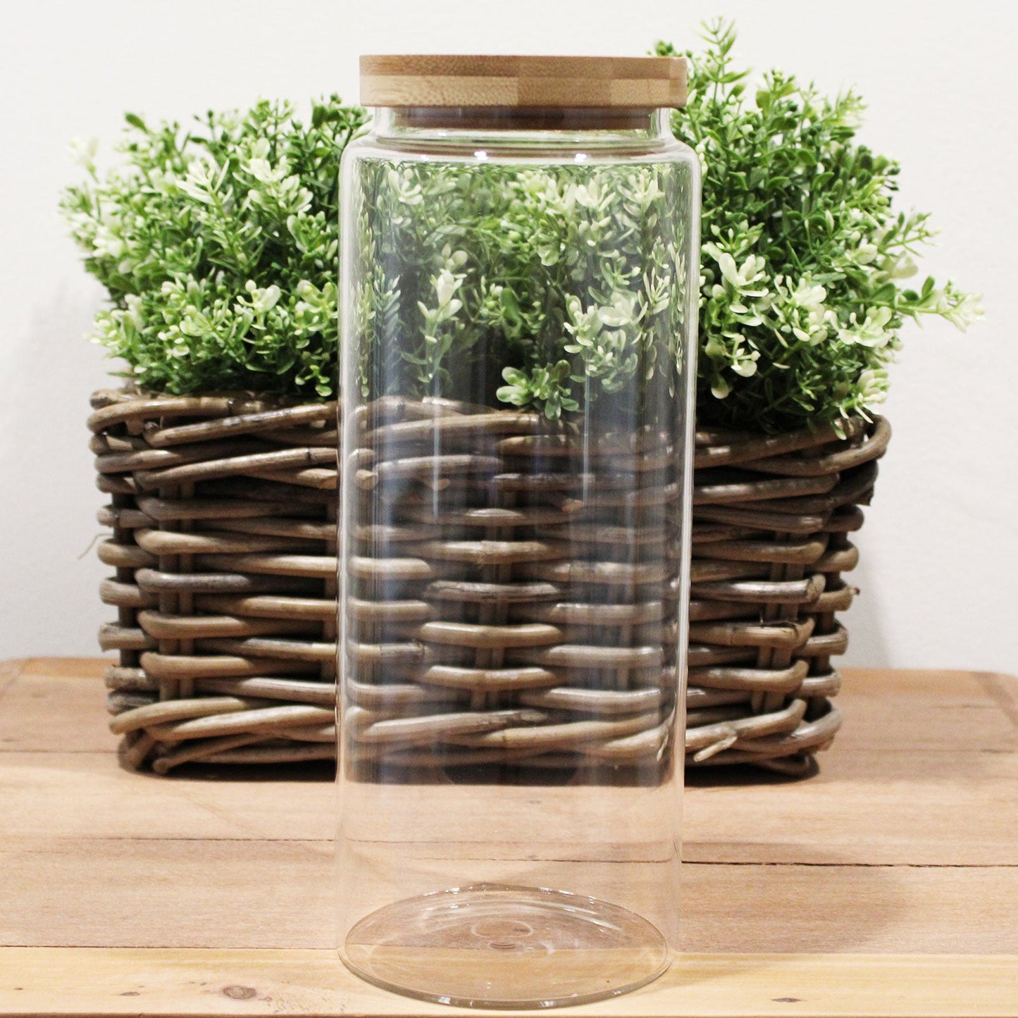 Cottage Bamboo Glass Jar with Bamboo Lid - 25 cm, tall empty clear jar standing before a woven planter of green foliage by Quintessential Holistic Health Ltd