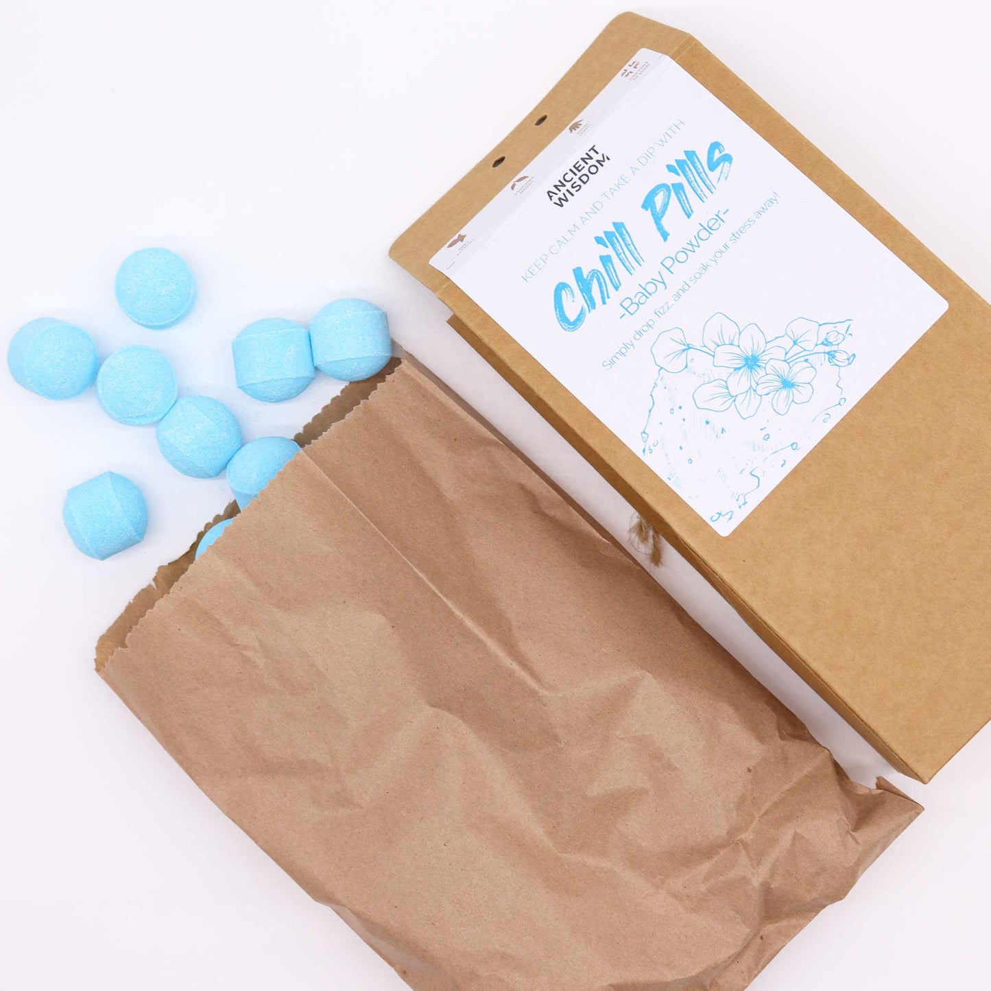 Vegan Bath Bomb Chill Pills Gift Pack - Baby Powder - 350g, open kraft box beside a paper bag and scattered pale blue tablets, by Quintessential Holistic Health Ltd