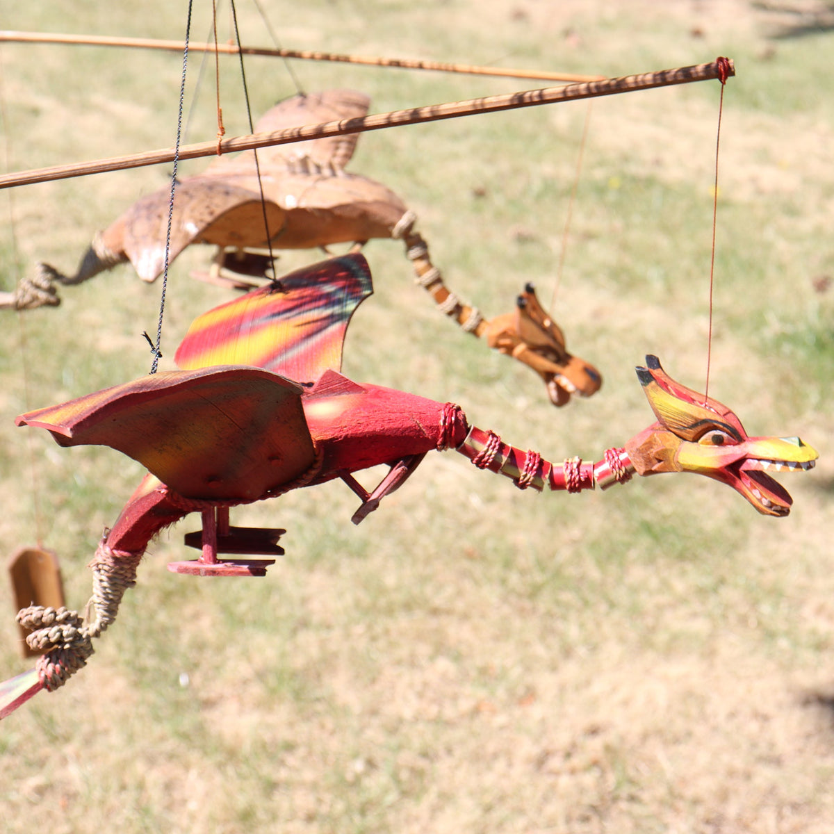 Handcrafted Coconut Shell Dragon Mobile - Red, hanging outdoors with its long jointed body and striped wings extended by Quintessential Holistic Health Ltd