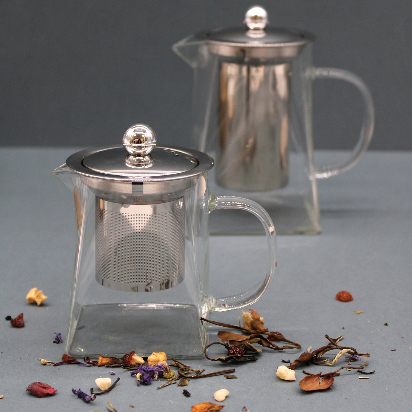 Tower-Shaped Glass Infuser Teapot - 350 ml, two clear pots with metal infusers and lids beside scattered dried botanicals by Quintessential Holistic Health Ltd
