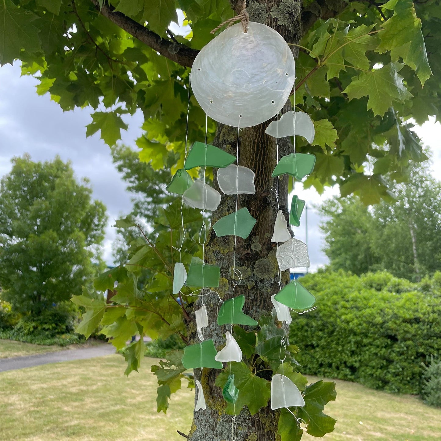 Recycled Glass Wind Chime - Green & White Glass Drop shown fully hanging among leafy tree branches by Quintessential Holistic Health Ltd