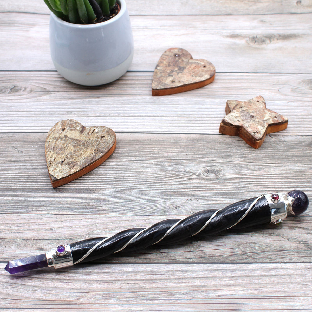 Handmade Twisted Teak Healing Wand - Silver Amethyst lying diagonally beside a plant pot and wooden ornaments by Quintessential Holistic Health Ltd