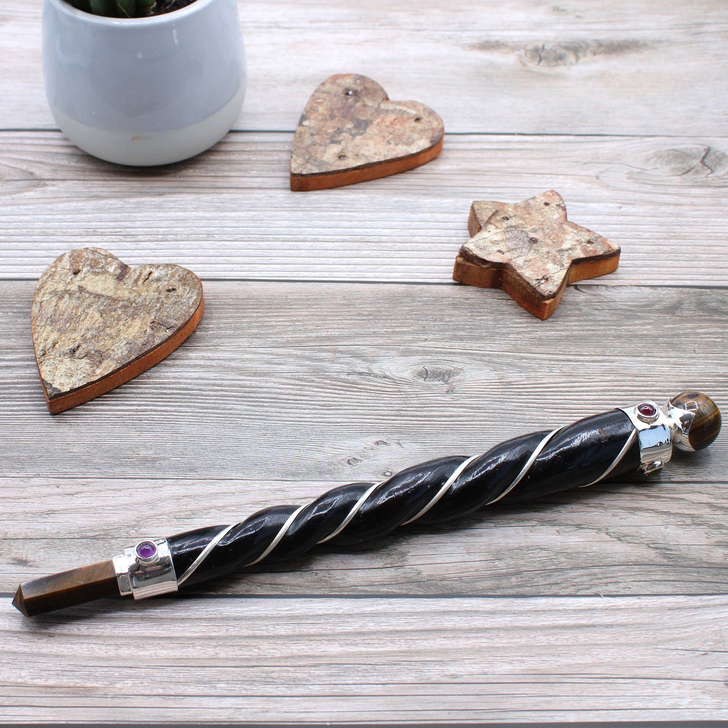 Handmade Twisted Teak Wand - Copper & Tiger's Eye Gemstone lying diagonally beside wooden heart and star ornaments by Quintessential Holistic Health Ltd
