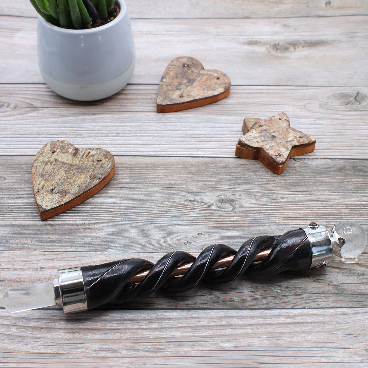 Spiral Teak Wood Healing Wand with Copper - Rock Quartz with dark spiral shaft and clear stone ends on a pale wooden surface by Quintessential Holistic Health Ltd