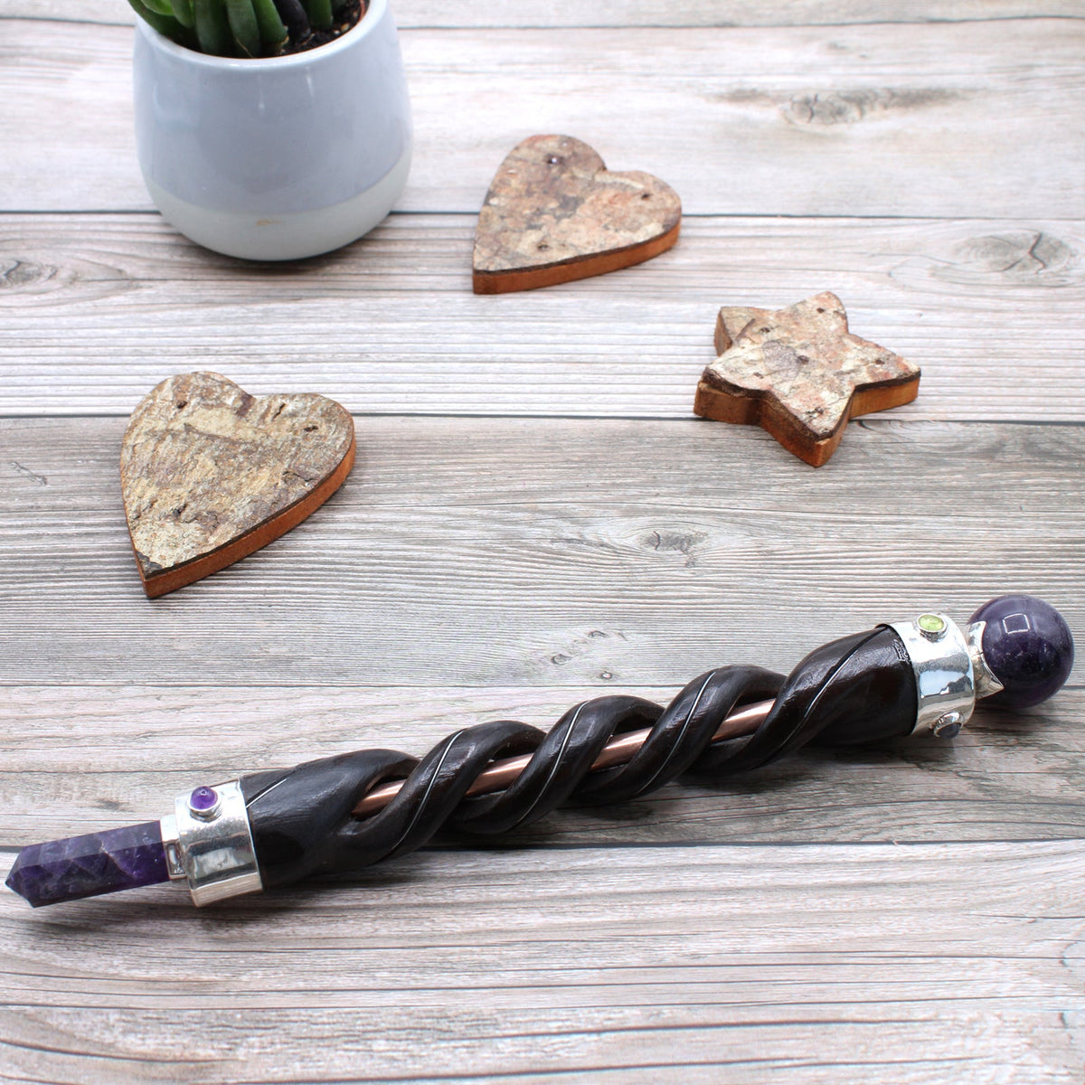 Spiral Teak Wood Healing Wand with Copper - Amethyst with dark spiral shaft and purple stone ends on a pale wooden surface by Quintessential Holistic Health Ltd