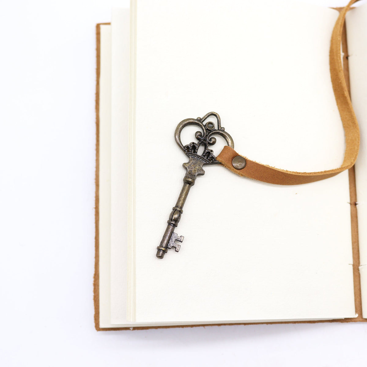 Oiled Leather 200-Page Notebook with Strap & Key – Medium Tan shown open with a metal key charm hanging over a blank page by Quintessential Holistic Health Ltd