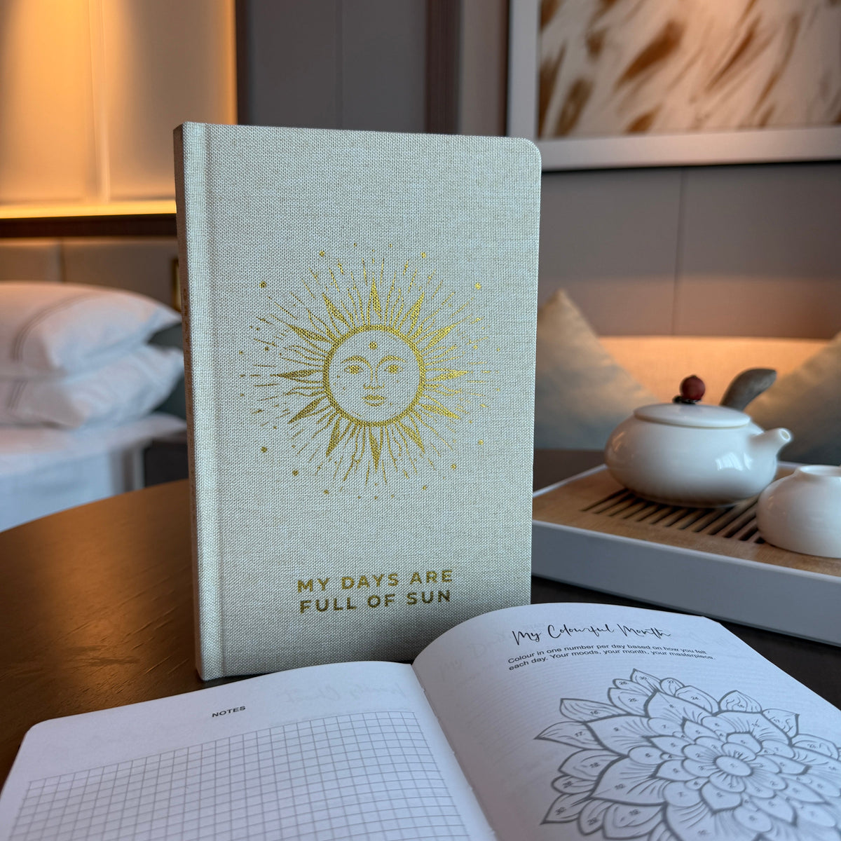 A5 Ivory Gold-Lined Gratitude Journal - My Days Are Full of Sun, standing upright beside an open page with a floral pattern, by Quintessential Holistic Health Ltd