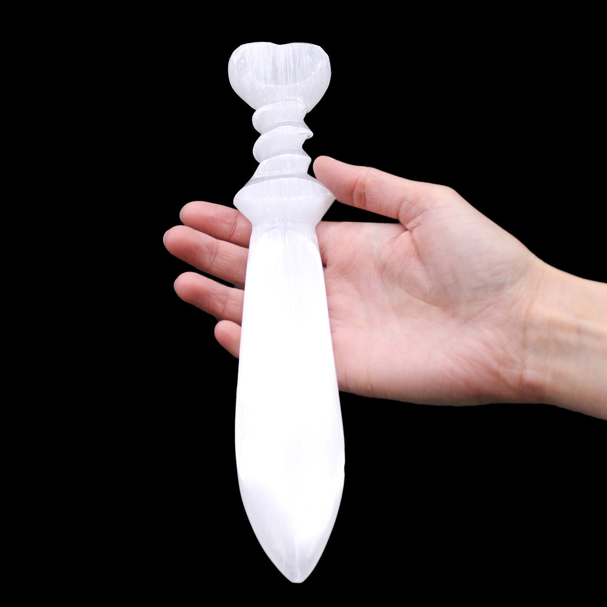 Handmade Large Spiral Selenite Ceremonial Knife - 25 × 4.5 cm, carved heart pommel and elongated pointed blade held beside a hand, by Quintessential Holistic Health Ltd