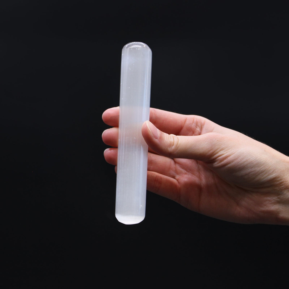 Rounded End Smooth Selenite Healing Wand held upright in one hand with its translucent white body visible by Quintessential Holistic Health Ltd