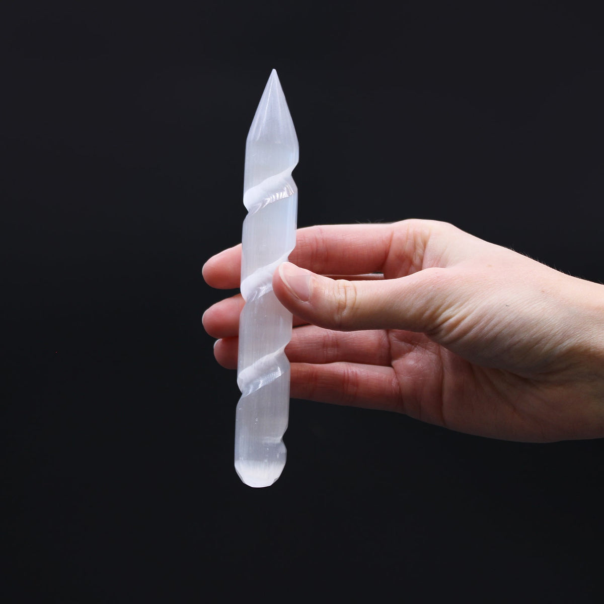 Pointed and Rounded End Selenite Spiral Healing Wand with a carved twist and pointed tip, held upright in one hand by Quintessential Holistic Health Ltd