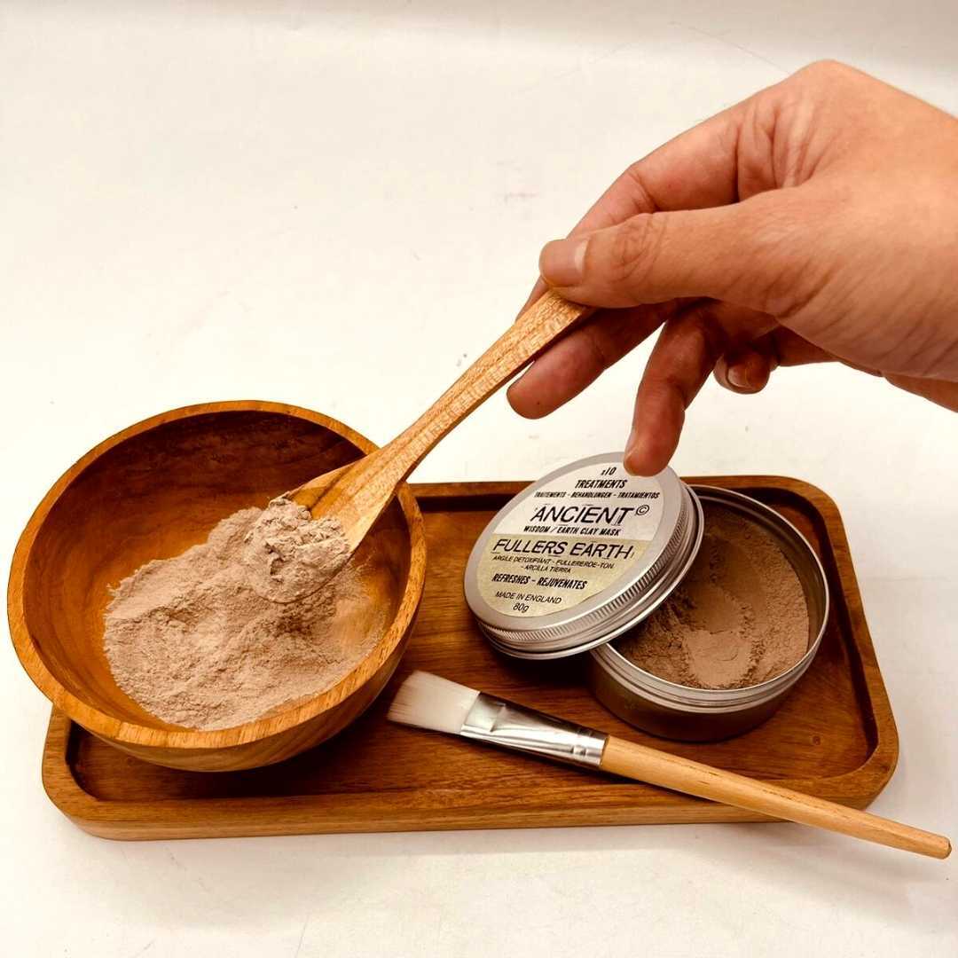 Handmade Teak Clay or Wax Spa Application Set with a hand holding a filled spoon above a bowl, tray, brush and two tins by Quintessential Holistic Health Ltd
