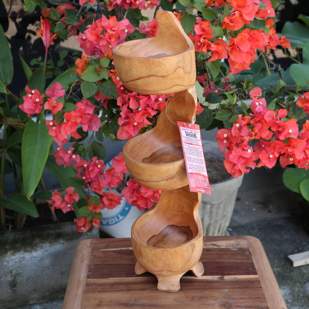 Hand-Carved Teak Root Three-Tier Standing Bowl, with three curved bowls, a twisting stem and square base among red flowers by Quintessential Holistic Health Ltd