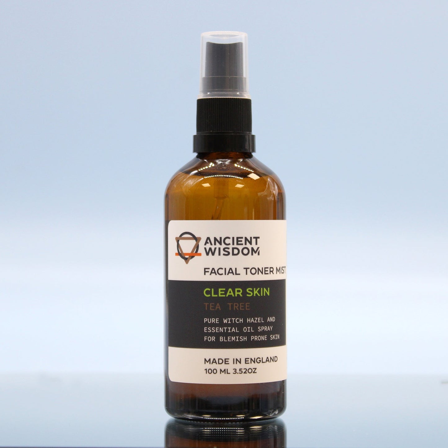 100ml Vegan-Friendly Witch Hazel Facial Toner Mist - Tea Tree in an amber spray bottle on a reflective block against pale blue by Quintessential Holistic Health Ltd