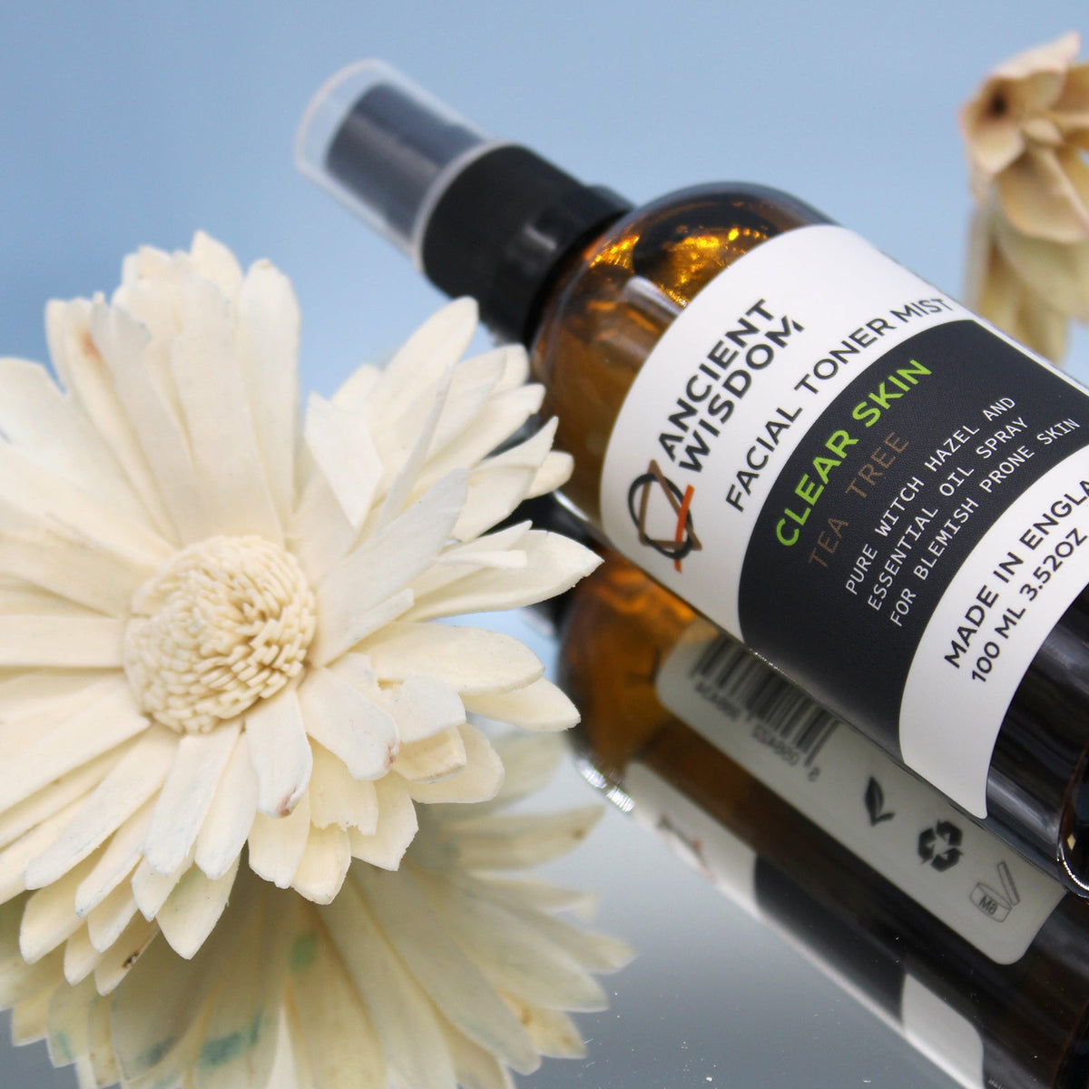 100ml Vegan-Friendly Witch Hazel Facial Toner Mist - Peppermint in an amber spray bottle lying beside a large white flower by Quintessential Holistic Health Ltd