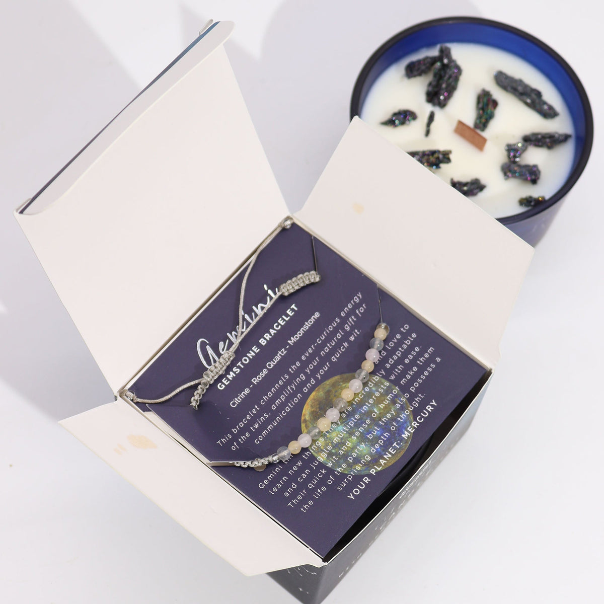 Gemini Zodiac Crystal Soy Wax Candle & Gemstone Bracelet, open Gemini box with a pale bracelet across the card and blue candle behind by Quintessential Holistic Health Ltd