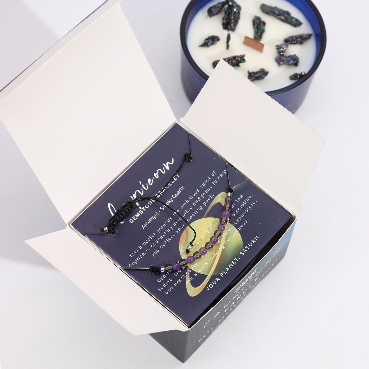 Capricorn Zodiac Crystal Soy Wax Candle & Gemstone Bracelet, open Capricorn box with a purple bracelet across the card and blue candle behind by Quintessential Holistic Health Ltd