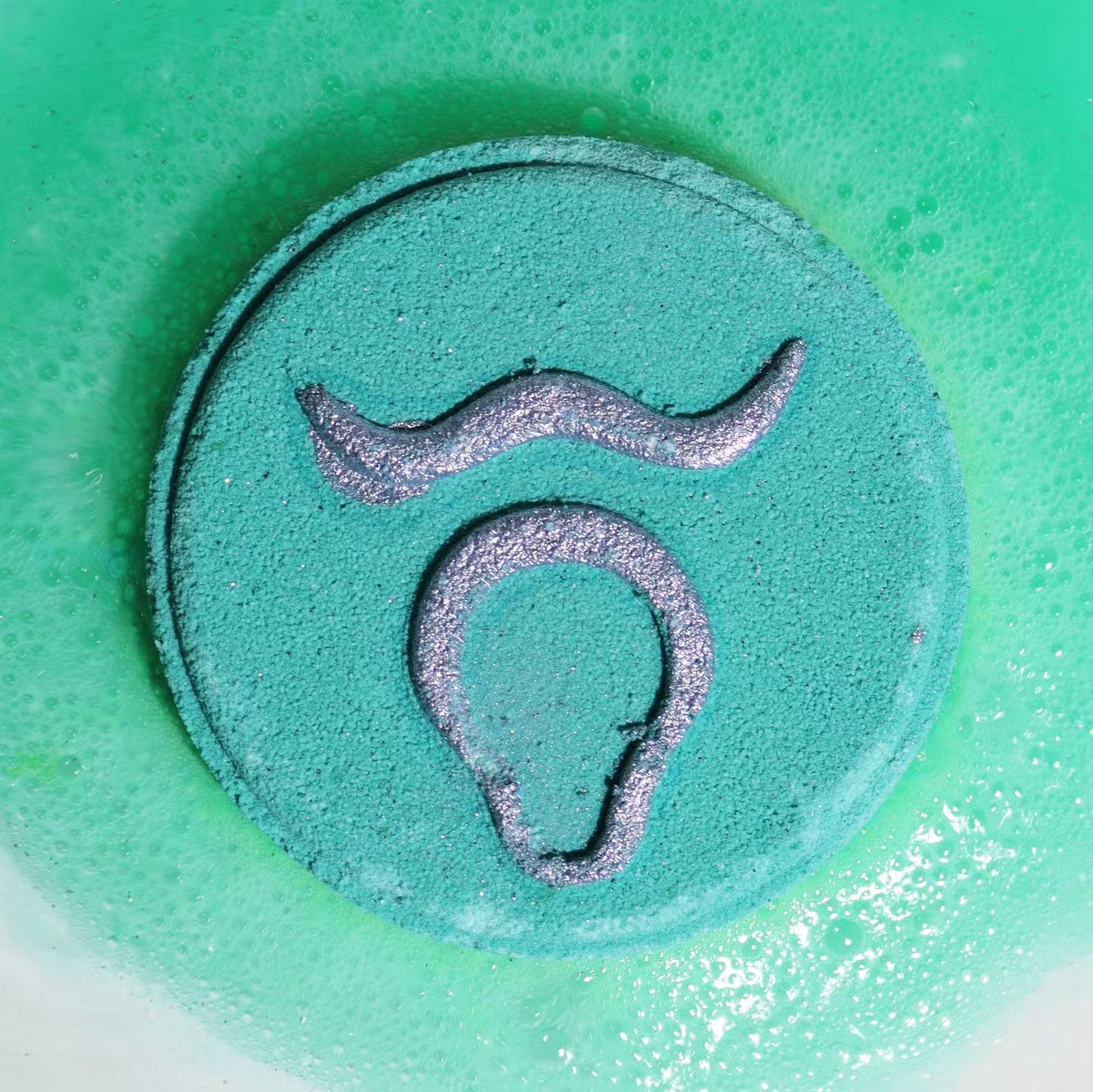 Fragranced Zodiac Horoscope Bath Bomb Fizzers - Taurus - 2 Pack, close-up of a turquoise fizzer embossed with the Taurus symbol by Quintessential Holistic Health Ltd