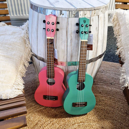 A Bright Pink and Turquoise Artisan Made Ukuleles leaning against a whitewash handmade barrel