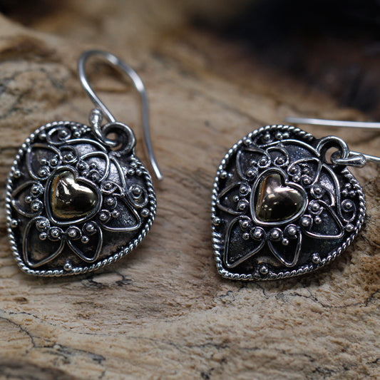 Close-up of handmade silver and gold heart-shaped earrings, featuring intricate mandala designs with a golden heart centrepiece
