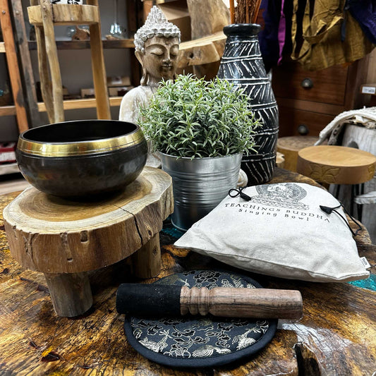 Side View of the 14 cm Hand Beaten & Engraved Singing Bowl Gift Set Sitting on a table surrounded by Buddha and decorative Spiritual Ornaments.