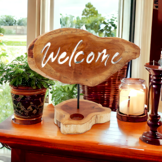 Welcome Cut out of a  Handmade Wooden Tea Light Candle Holder Sign on Display on a Unit Surrounded by other Ornaments and Candles