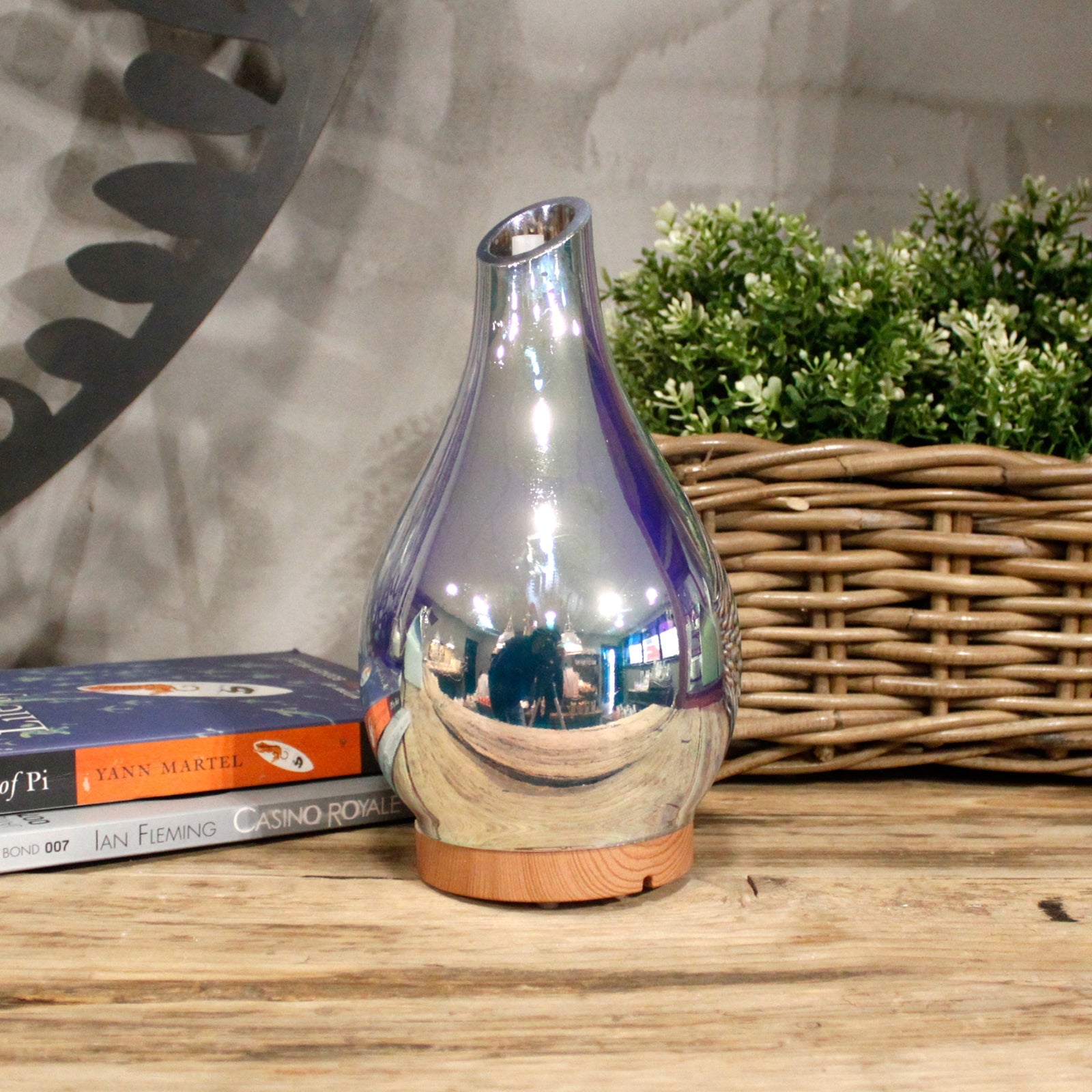 Colour-Changing USB Aroma Diffuser - Ibiza with a reflective silver teardrop body beside books and a woven planter by Quintessential Holistic Health Ltd