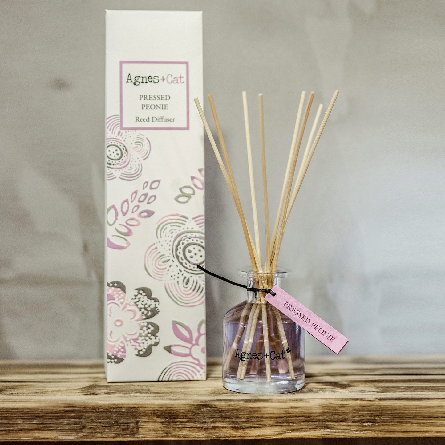 Reed Diffuser - Pressed Peony Rose - 140ml, purple-tinted bottle with natural-coloured reeds beside a pink-patterned box by Quintessential Holistic Health Ltd