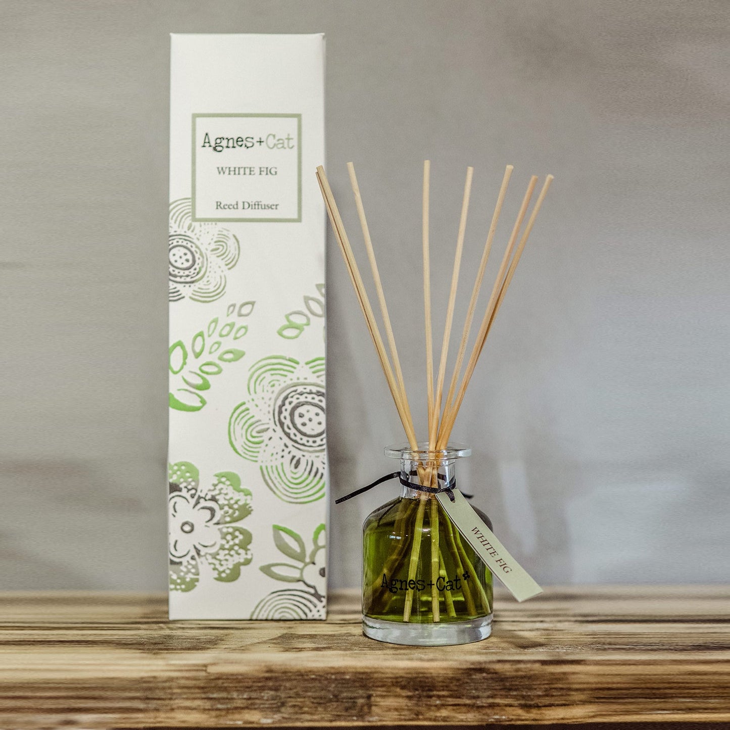 Reed Diffuser - White Fig - 140ml, green-tinted bottle with pale reeds beside a green floral box on a wooden surface, by Quintessential Holistic Health Ltd
