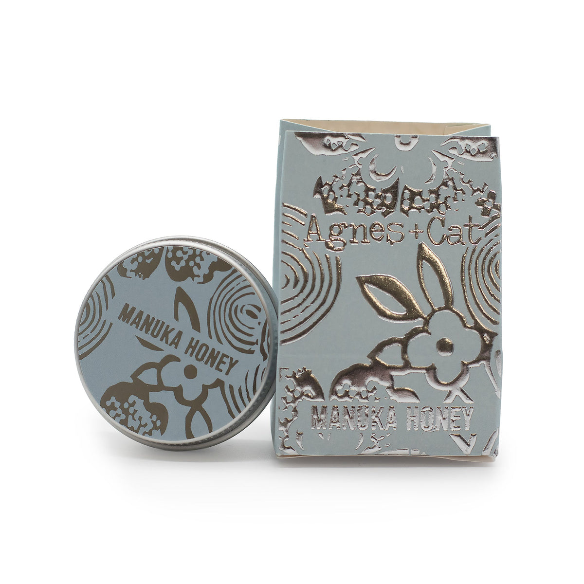 Hand-Poured Vegan-Friendly Natural Lip Balm - Manuka Honey, with a silver-grey illustrated tin beside a matching box, by Quintessential Holistic Health Ltd