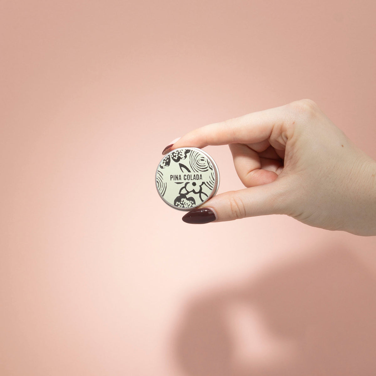 Hand-Poured Vegan-Friendly Natural Lip Balm - Pina Colada in a pale patterned tin held between fingers by Quintessential Holistic Health Ltd