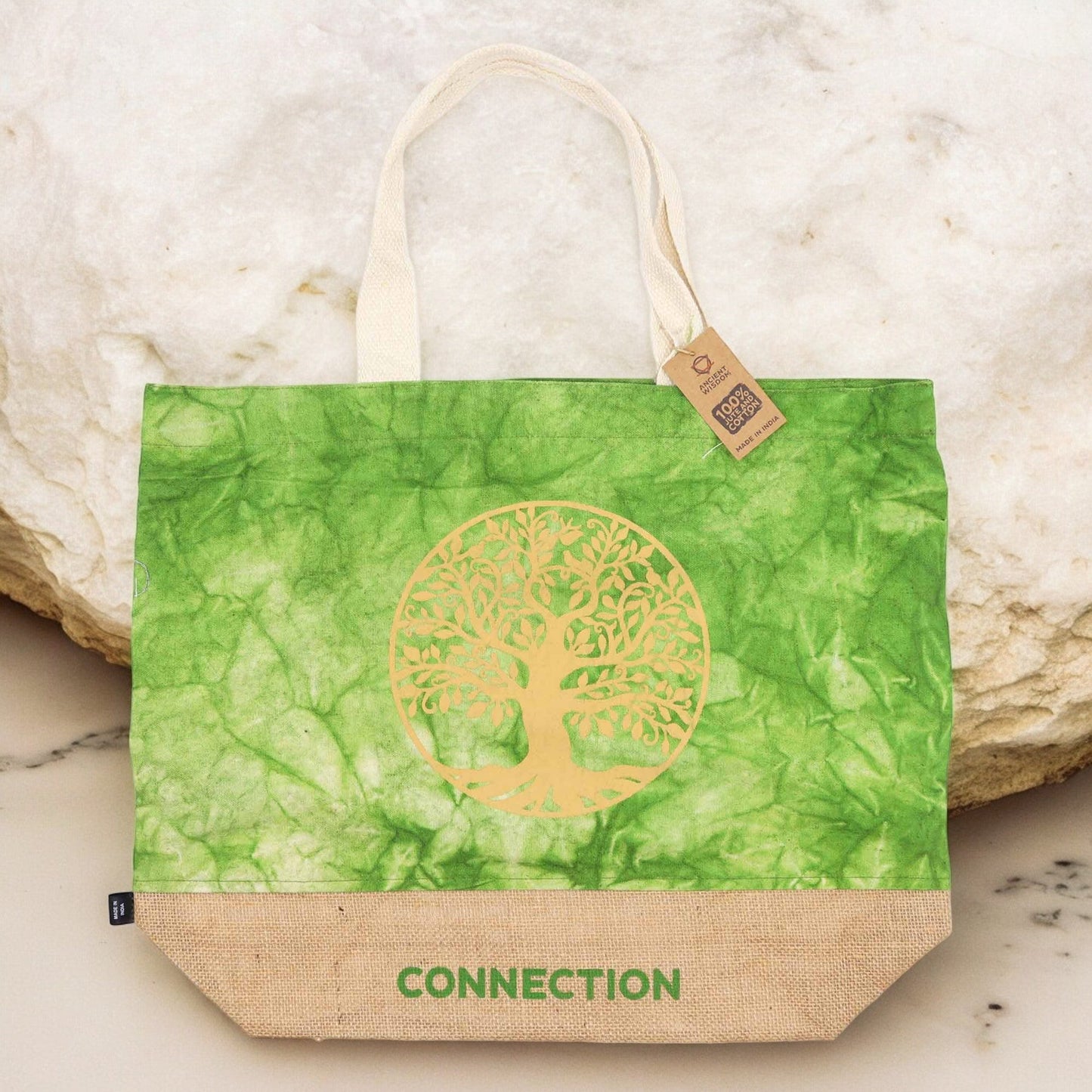 Green Stonewash Jute & Cotton Tote Bag - Tree of Life Connection standing against pale rocks with its gold tree design visible by Quintessential Holistic Health Ltd