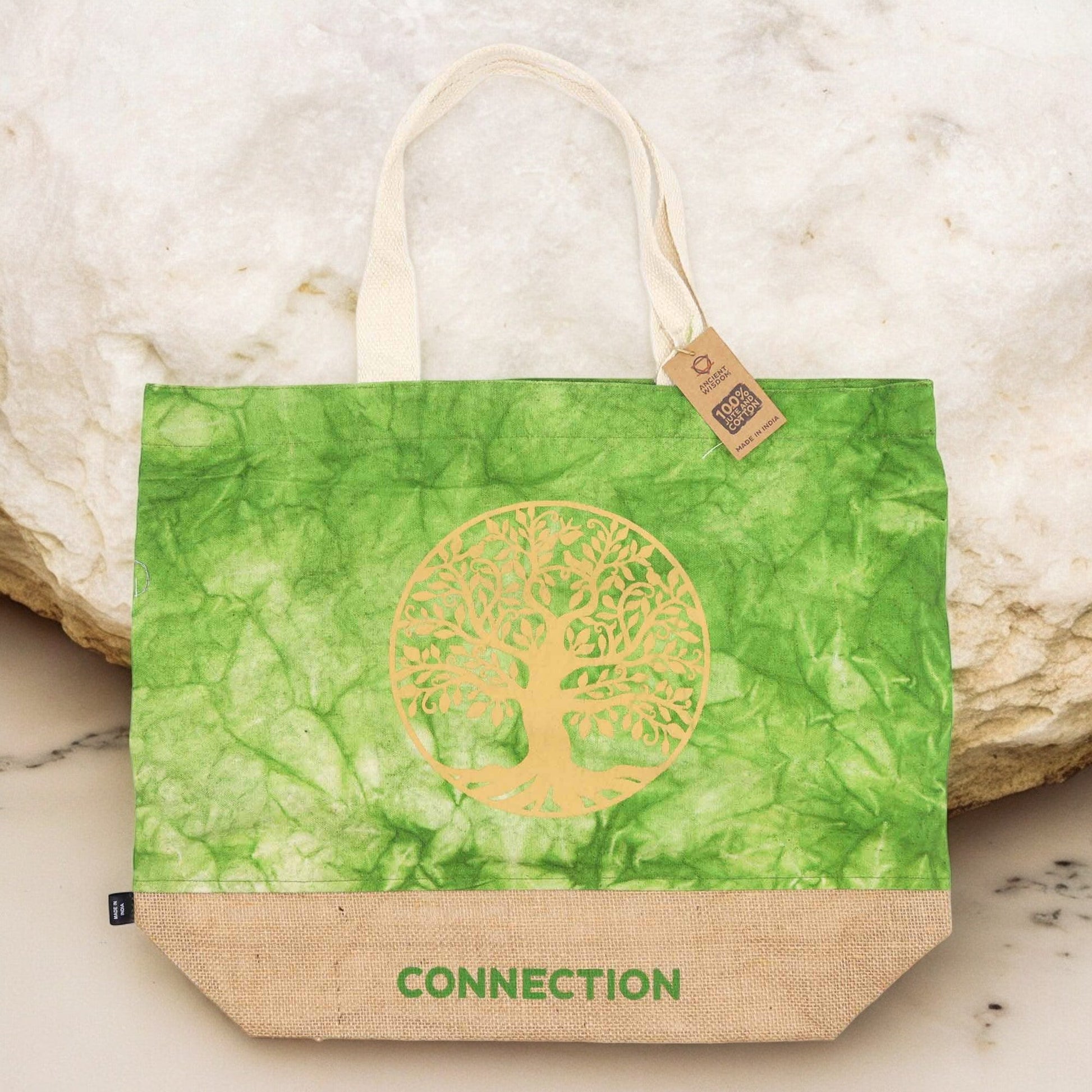 Green Stonewash Jute & Cotton Tote Bag - Tree of Life Connection standing against pale rocks with its gold tree design visible by Quintessential Holistic Health Ltd