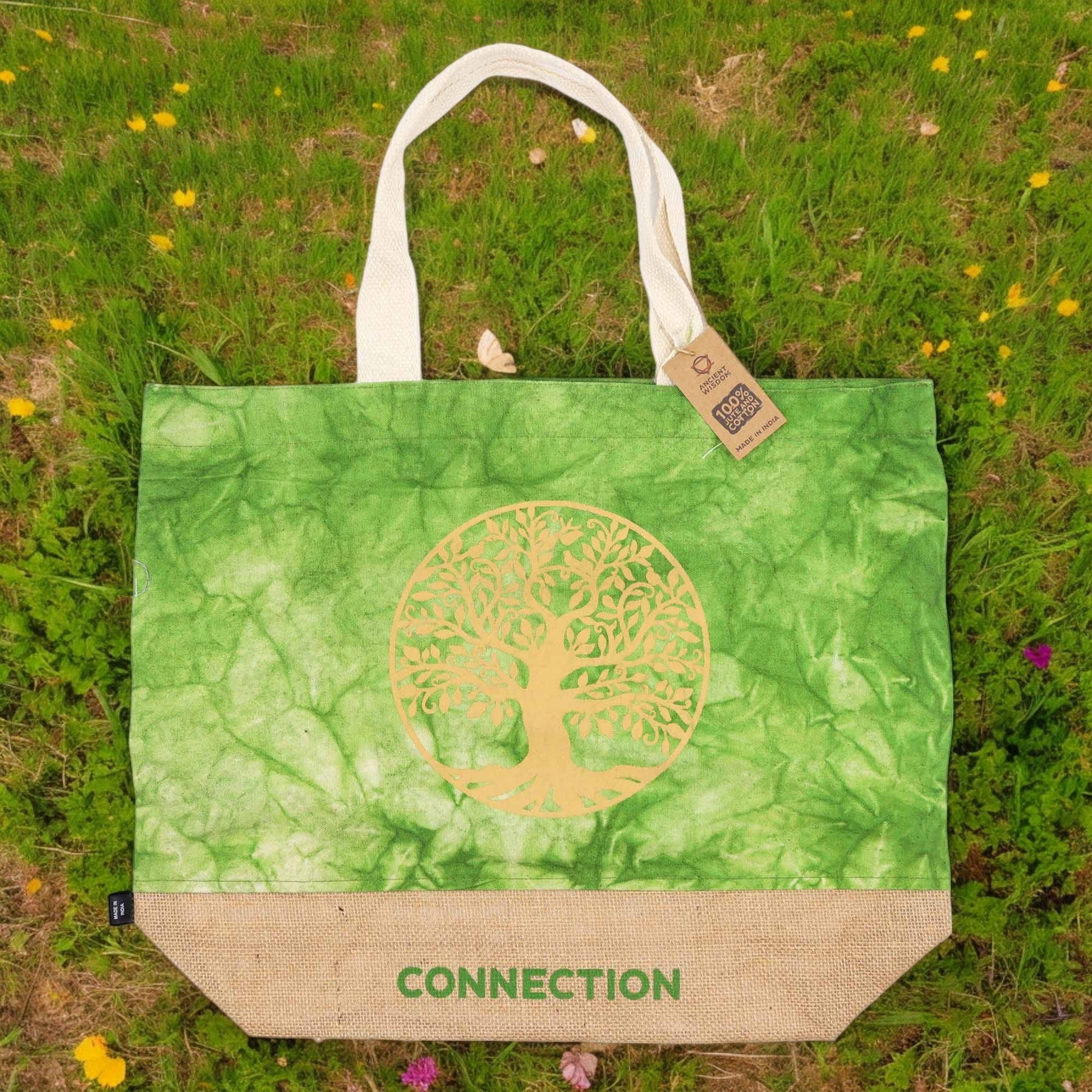 Green Stonewash Jute & Cotton Tote Bag - Tree of Life Connection displayed upright on grass among small yellow flowers by Quintessential Holistic Health Ltd