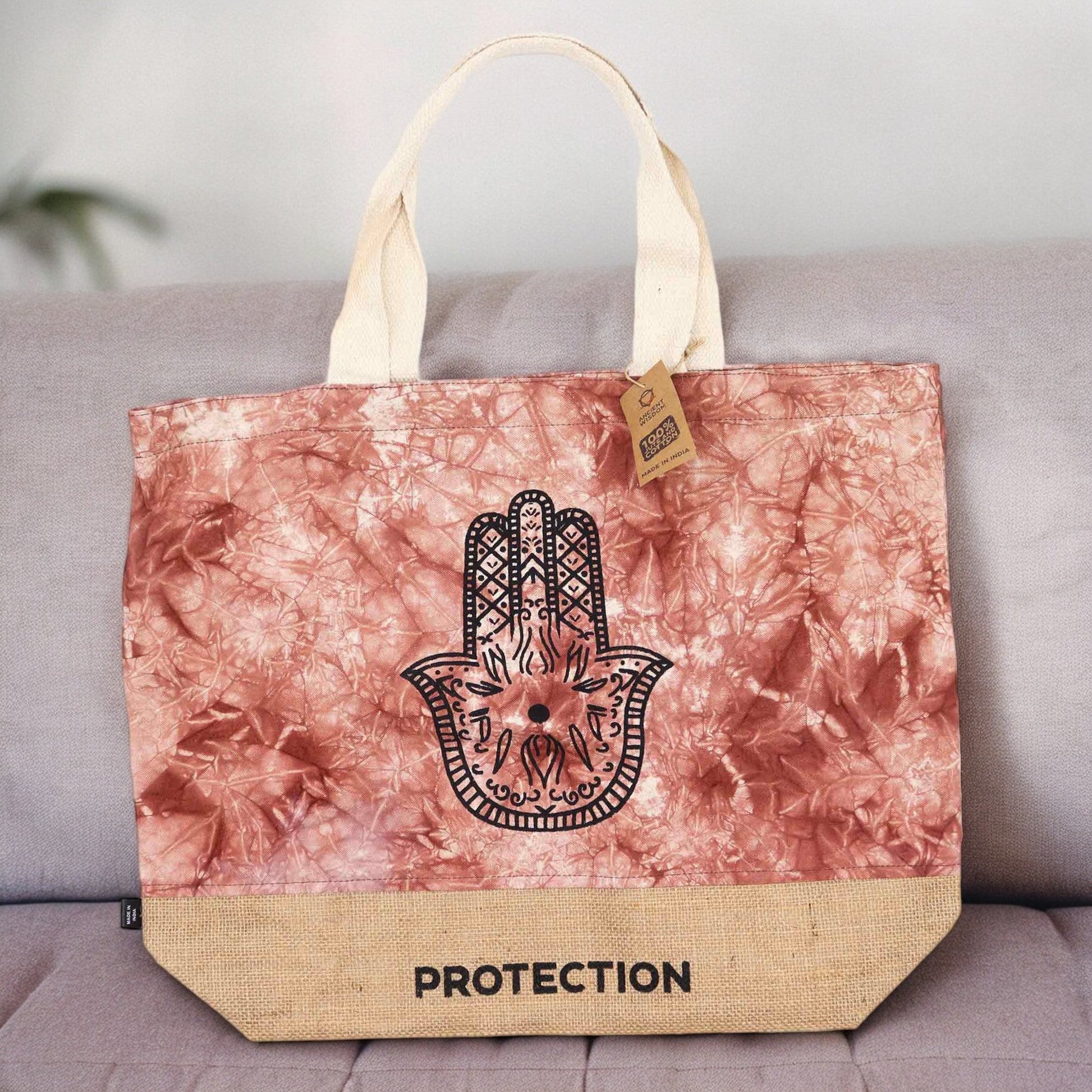 Terracotta Stonewash Jute & Cotton Tote - Hamsa Protection displayed upright on a grey cushioned seat with its black Hamsa design visible by Quintessential Holistic Health Ltd