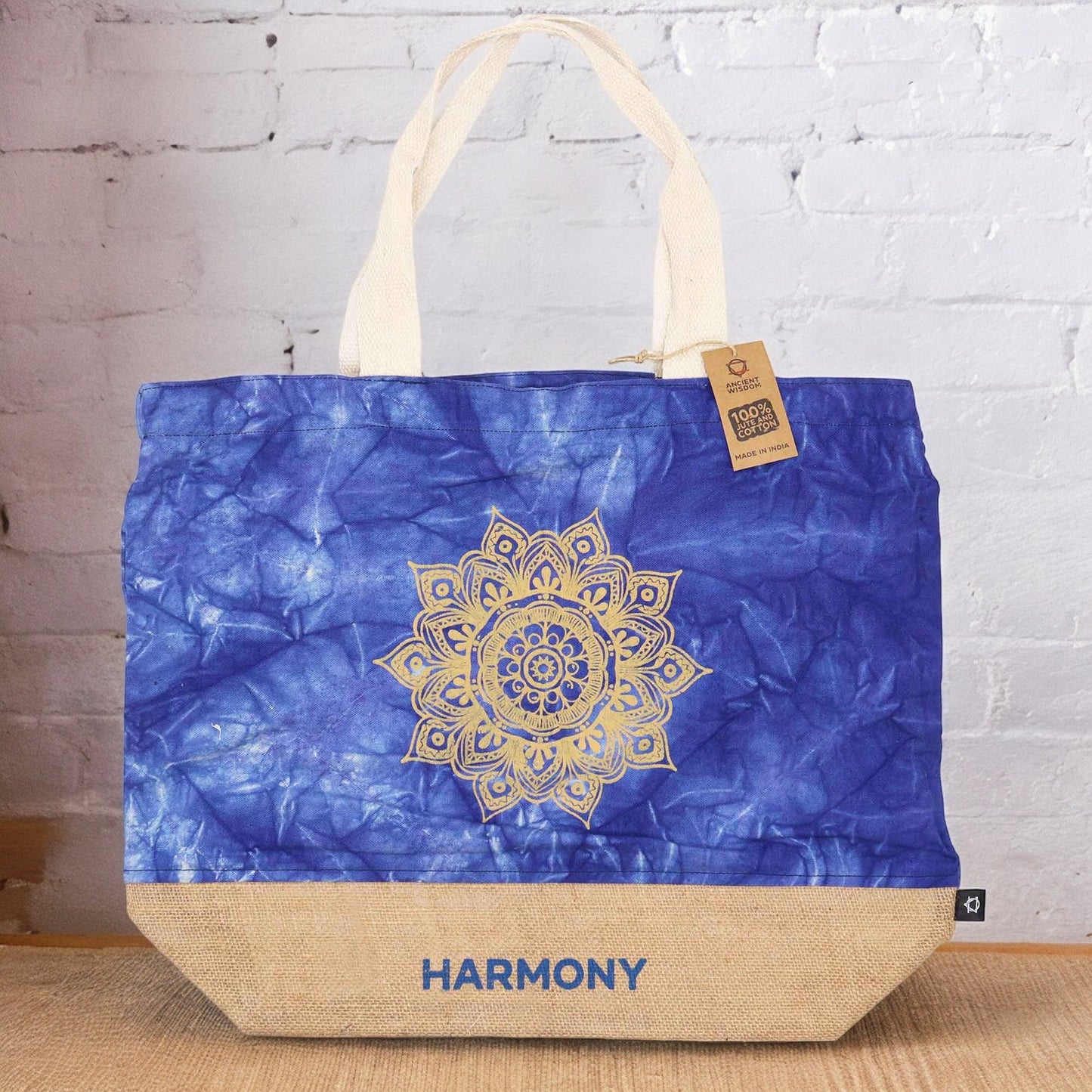 Blue Stonewash Jute & Cotton Tote Bag - Mandala - Harmony standing against a white brick wall with its gold mandala design visible by Quintessential Holistic Health Ltd