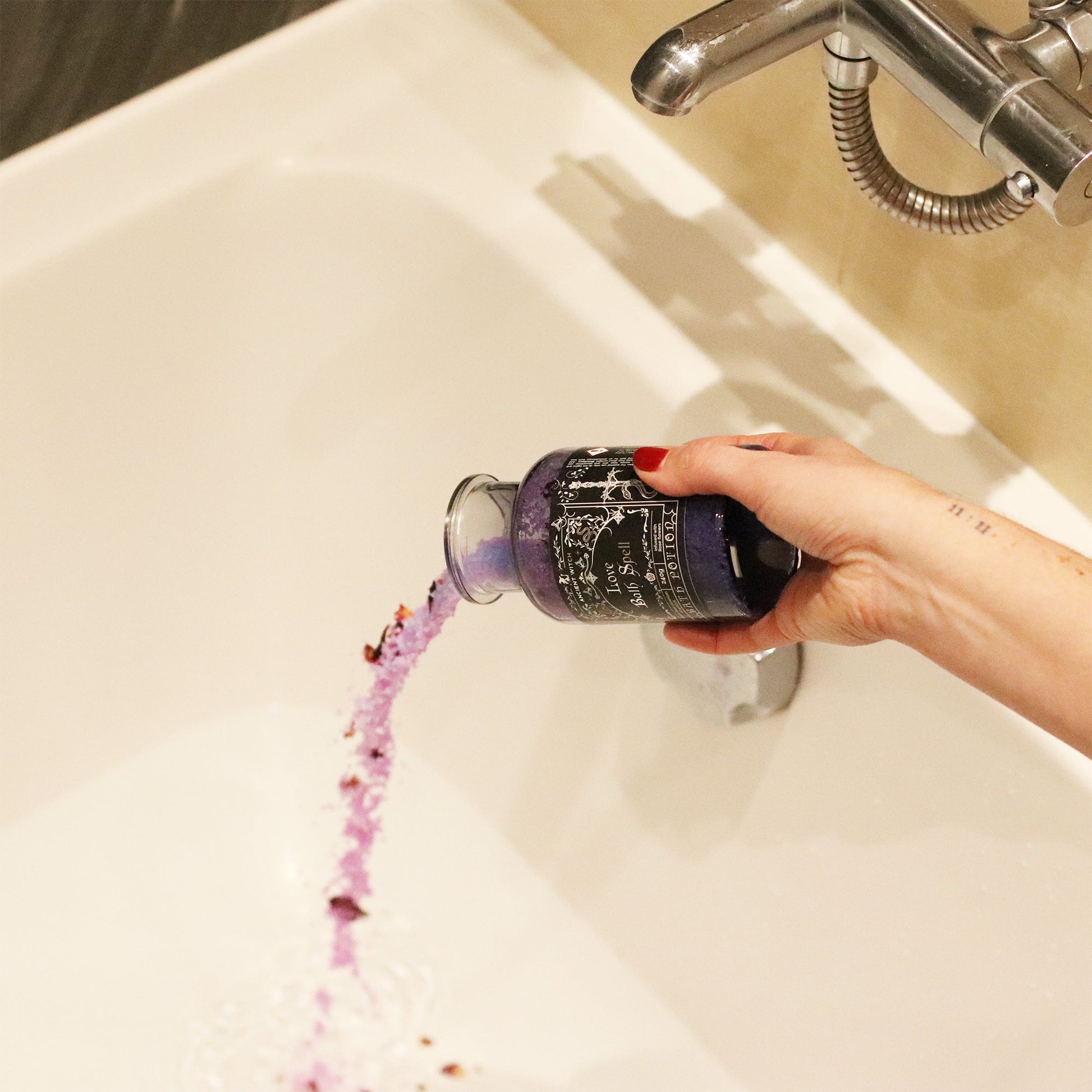 Vegan Bath Spell Potion & Rose Quartz Crystal Amulet - Love, held over a white bath as purple grains and petals pour out by Quintessential Holistic Health Ltd