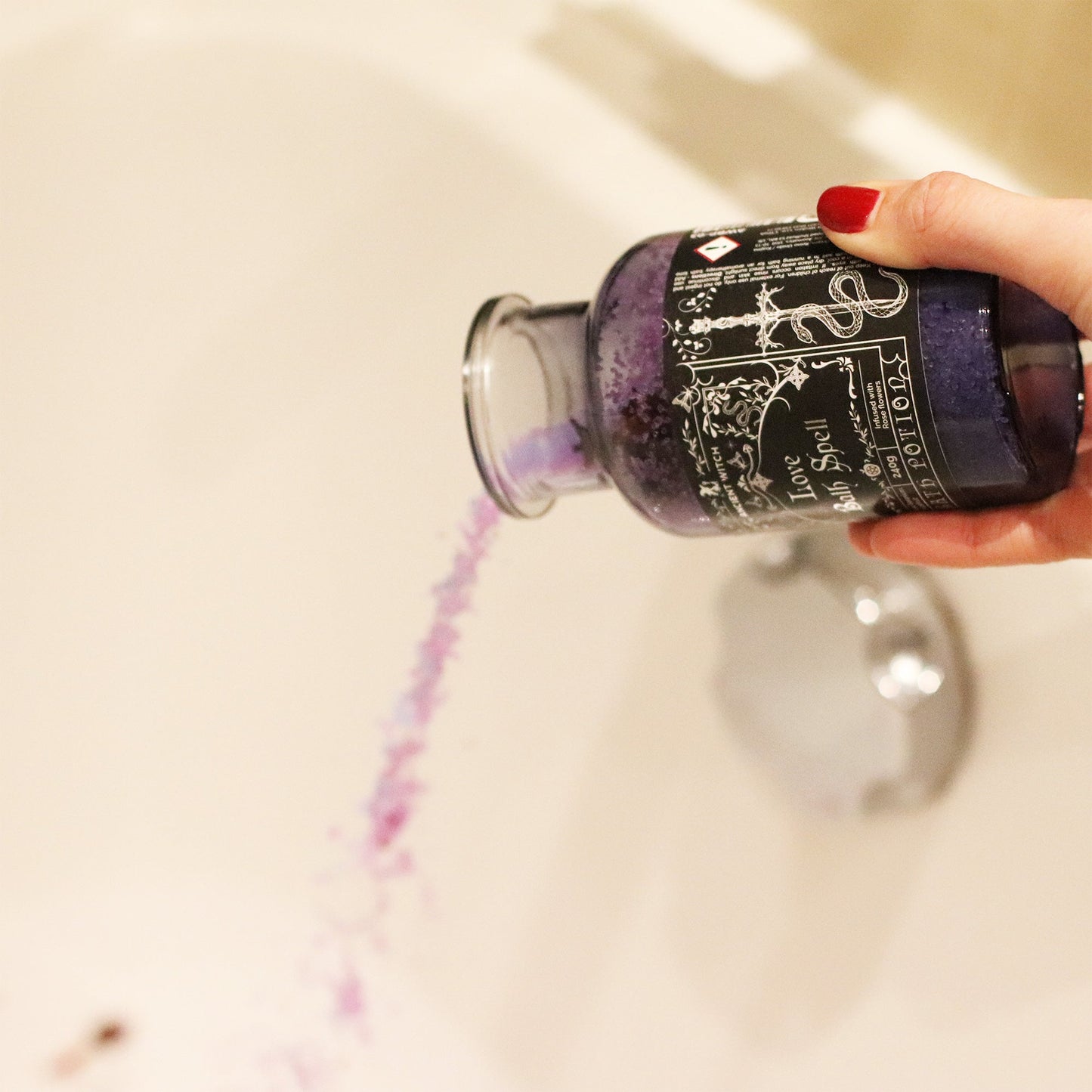 Vegan Bath Spell Potion & Rose Quartz Crystal Amulet - Love, tilted over a white bath as a stream of purple grains pours out by Quintessential Holistic Health Ltd