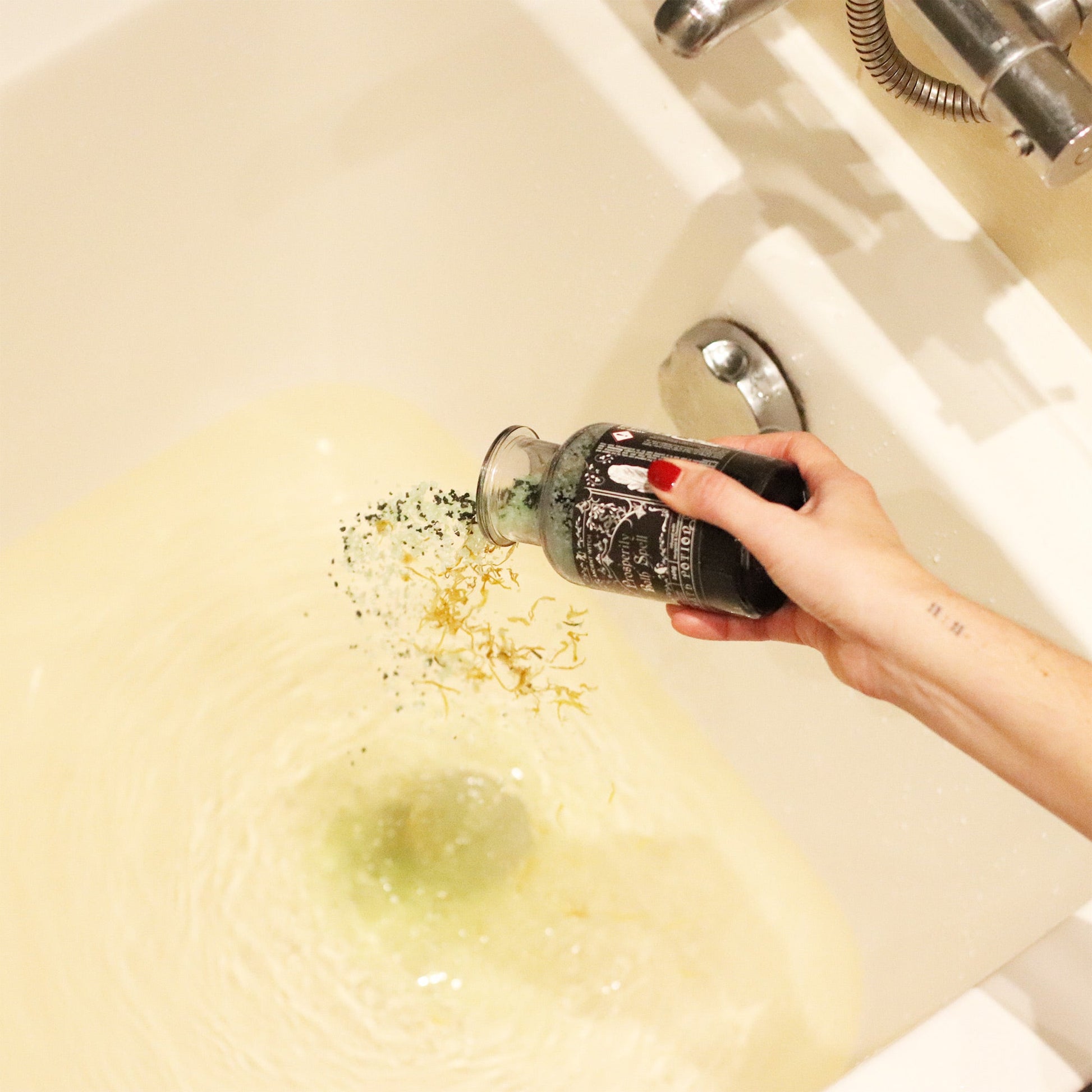 Vegan Bath Spell Potion & Aventurine Crystal Amulet - Prosperity, poured by a hand with red nails into pale green bathwater, by Quintessential Holistic Health Ltd