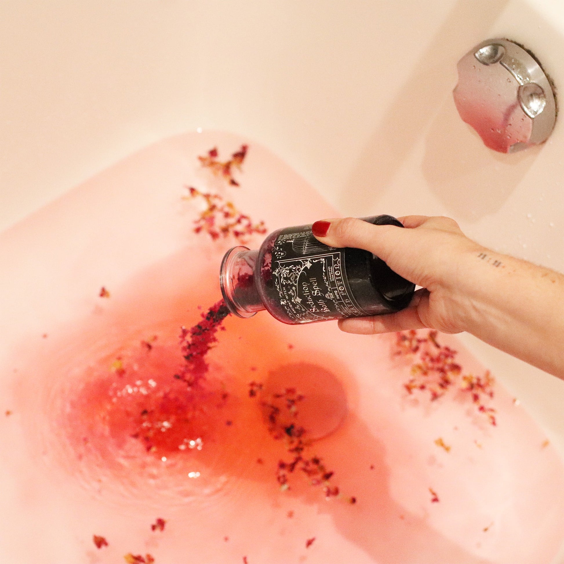 Vegan Bath Spell Potion & Amethyst Crystal Amulet - Seduction, bottle pouring dark grains into pink bathwater with floating petals, by Quintessential Holistic Health Ltd