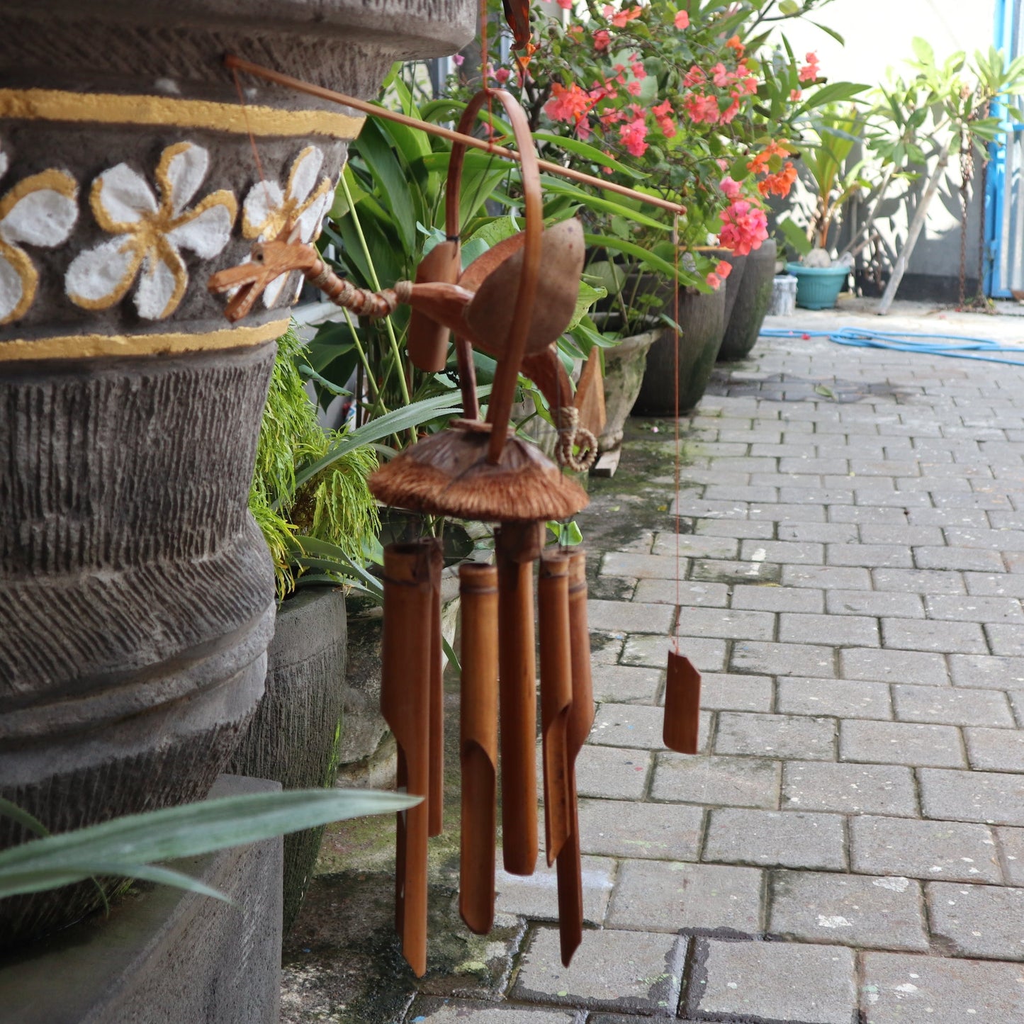 Handcrafted Bamboo Wind Chime - Natural - Dragon hanging among green plants with a carved dragon above brown tubes by Quintessential Holistic Health Ltd