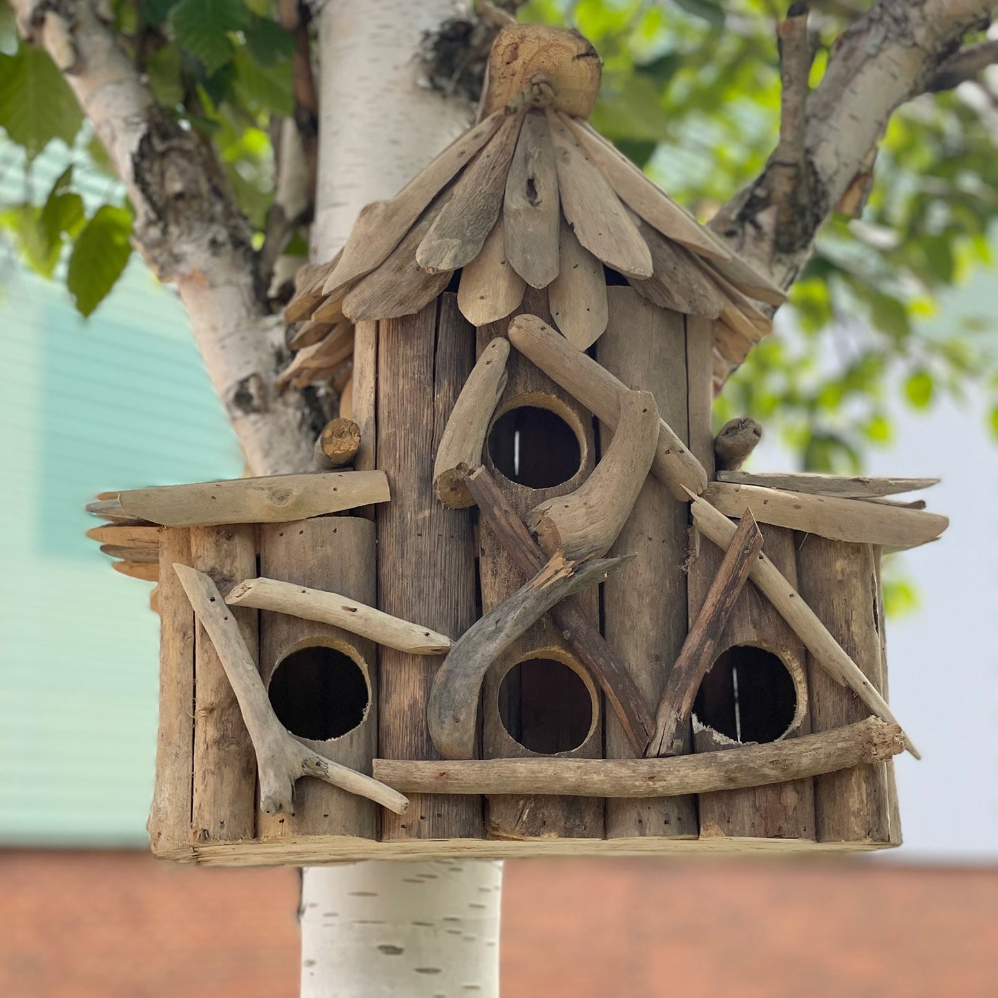 Handmade Recycled Driftwood Bird Box - Croft, displayed on a tree with four round openings and a pointed central roof, by Quintessential Holistic Health Ltd