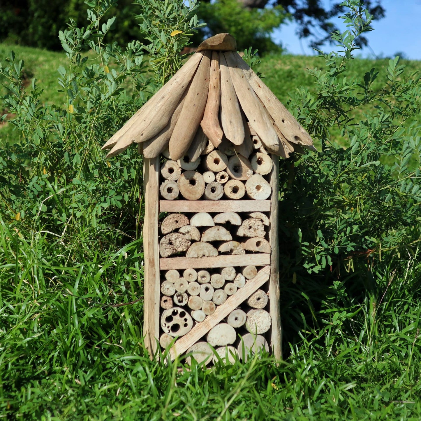 Handmade Recycled Driftwood Bee and Insect Tall House, displayed outdoors with filled sections, a diagonal brace and pitched roof, by Quintessential Holistic Health Ltd