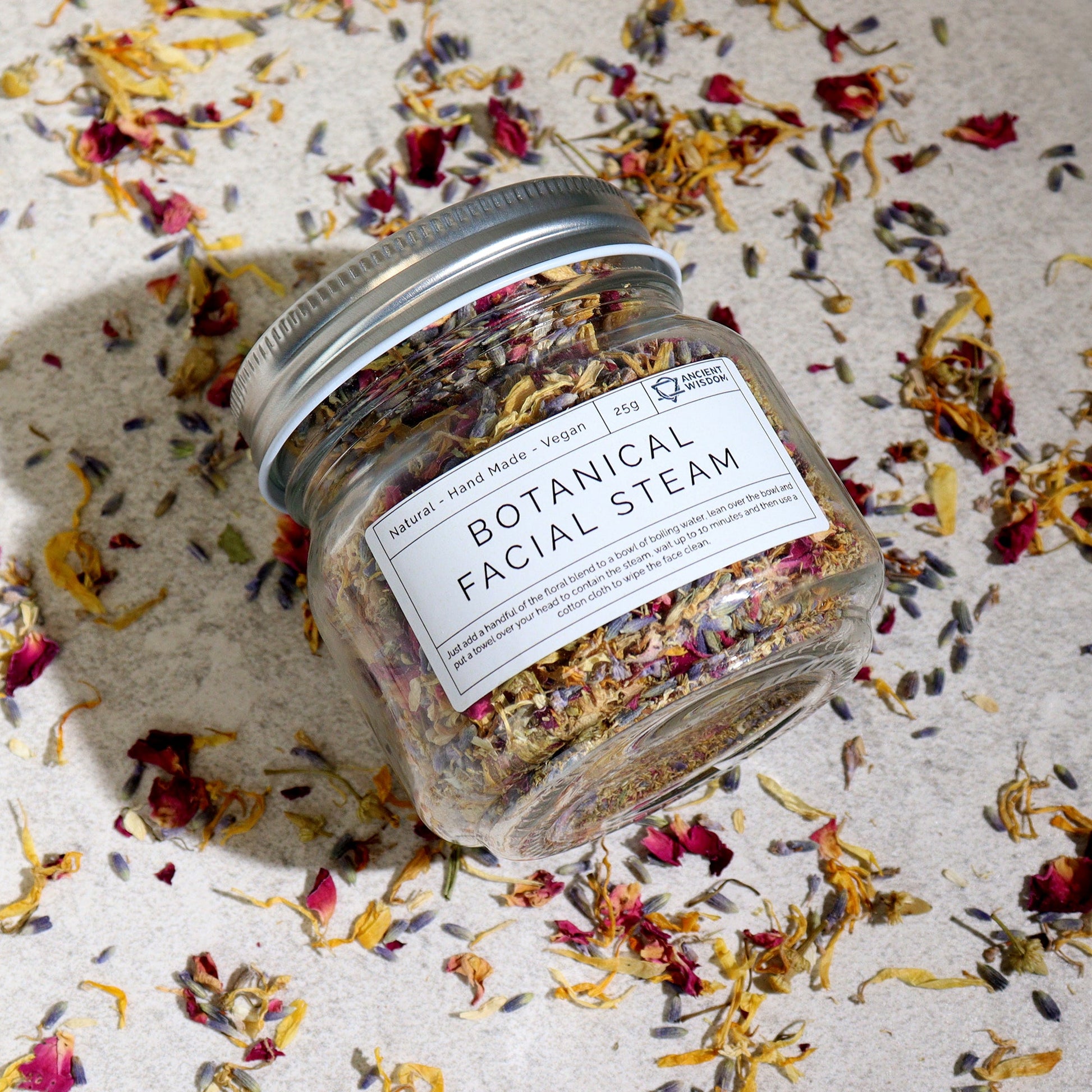Natural Floral Bath Soak - 140g, tilted labelled glass jar among scattered yellow and red dried petals, by Quintessential Holistic Health Ltd