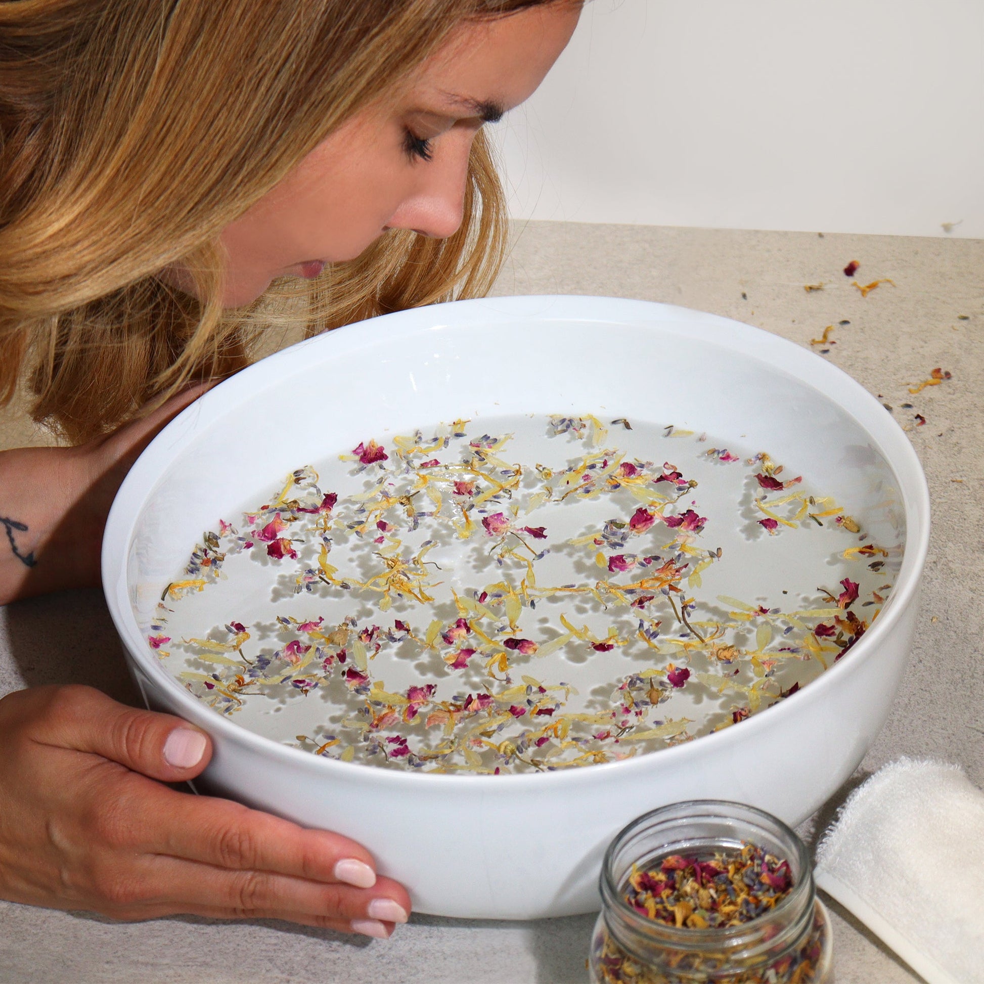 Natural Floral Bath Soak - 140g, woman holding a white bowl of milky water scattered with colourful dried petals, by Quintessential Holistic Health Ltd