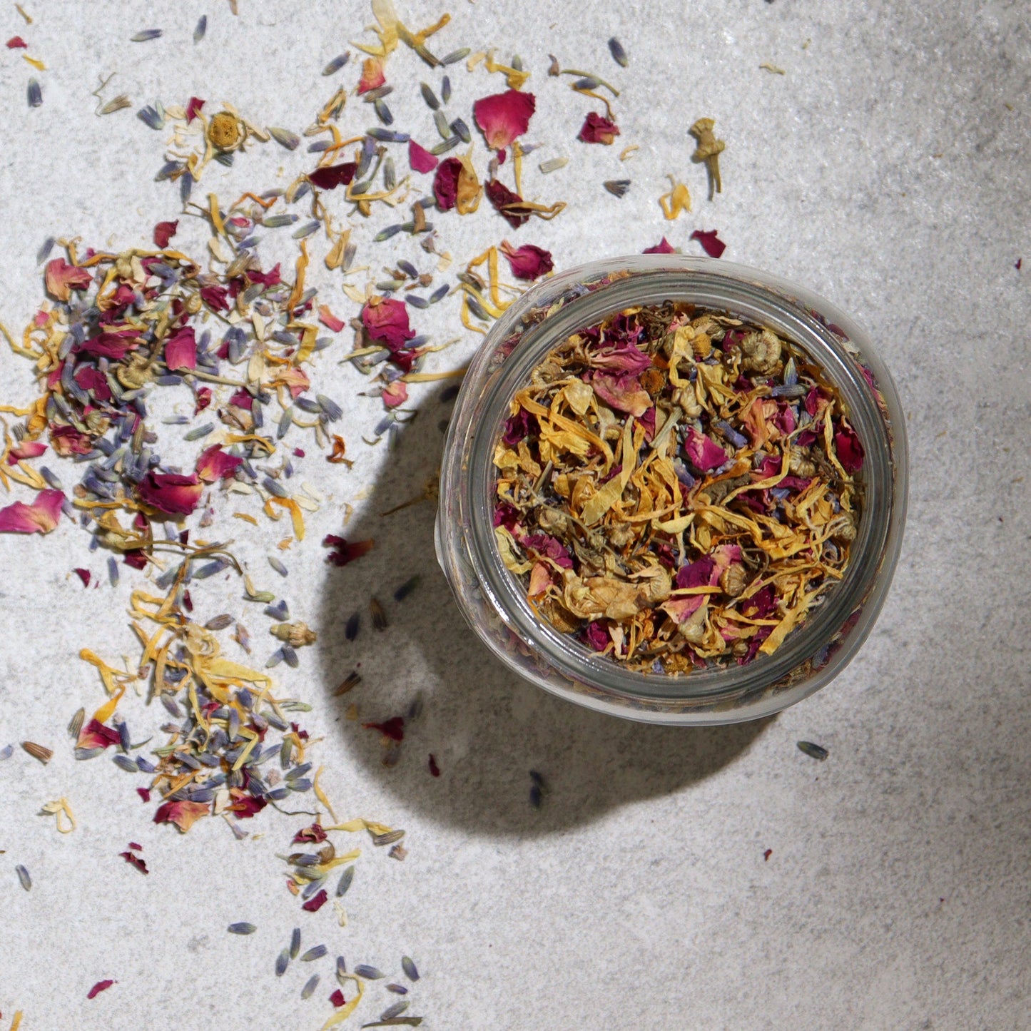 Natural Floral Bath Soak - 140g, open glass jar surrounded by scattered colourful dried petals, by Quintessential Holistic Health Ltd